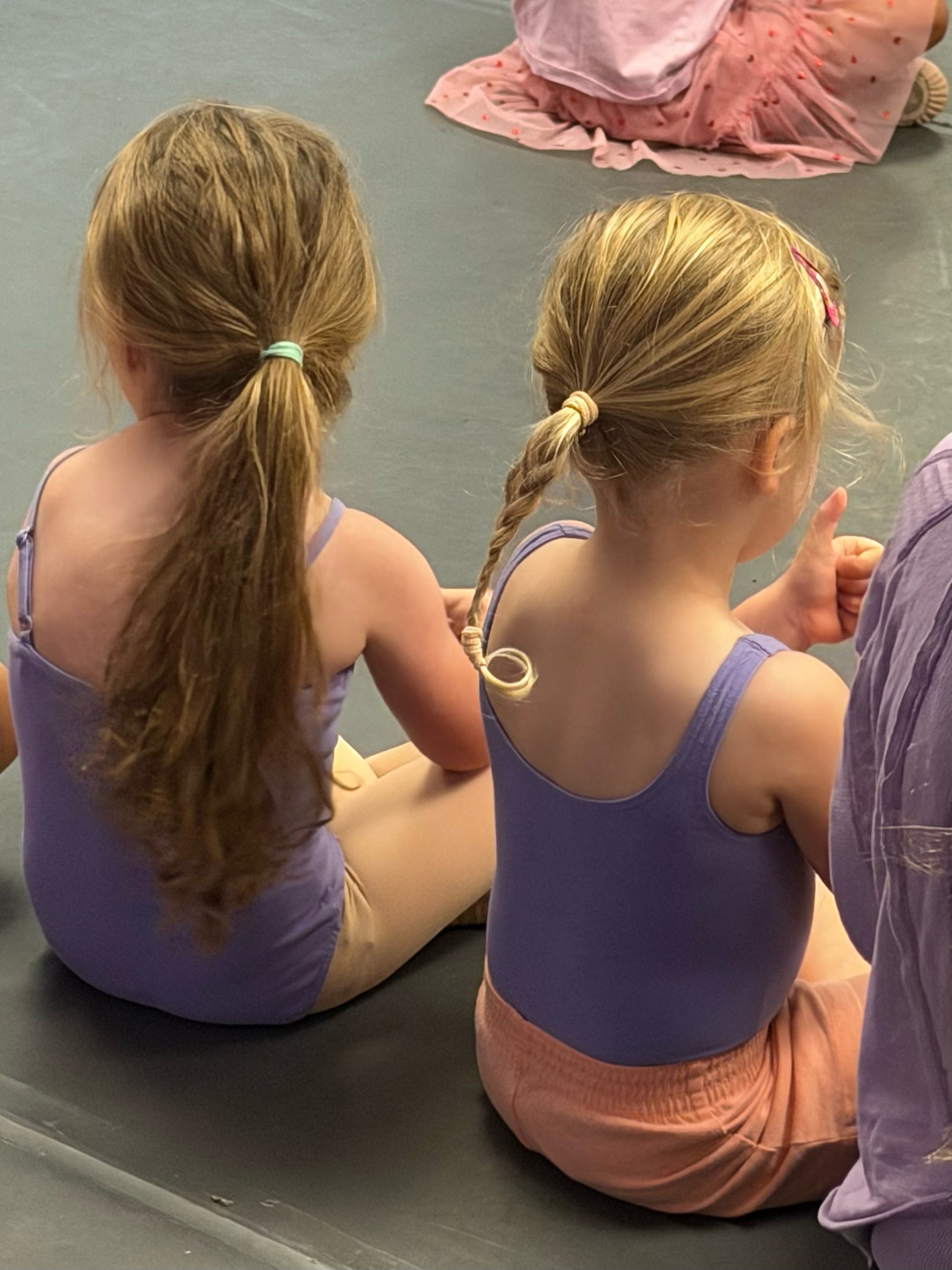 Two preschool Dance Connections dancers in purple leotards sitting together in class